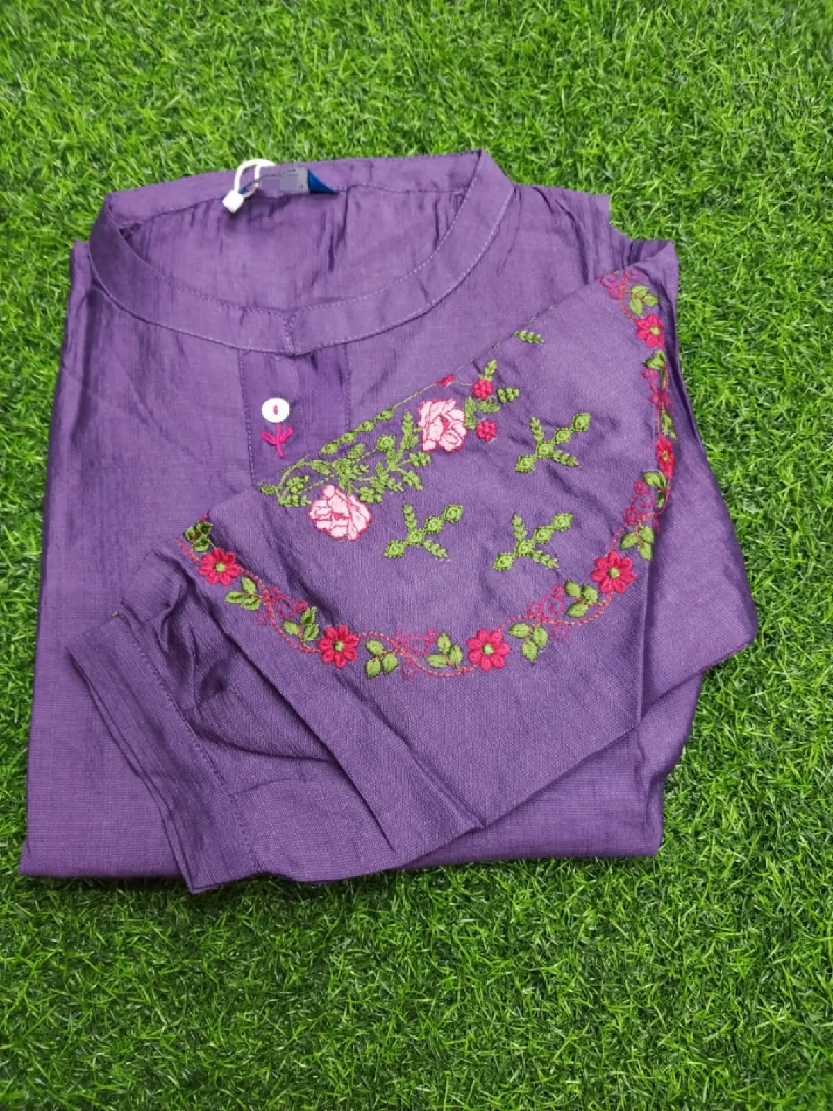 Folded purple garment with floral embroidery on a grassy background