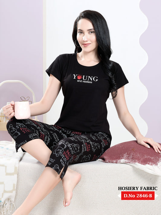 Woman wearing a black outfit with text, sitting on a couch holding a cup.