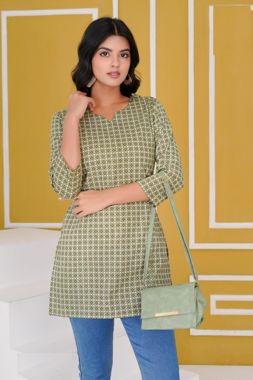 Woman wearing a green patterned dress with a matching handbag against a yellow wall.