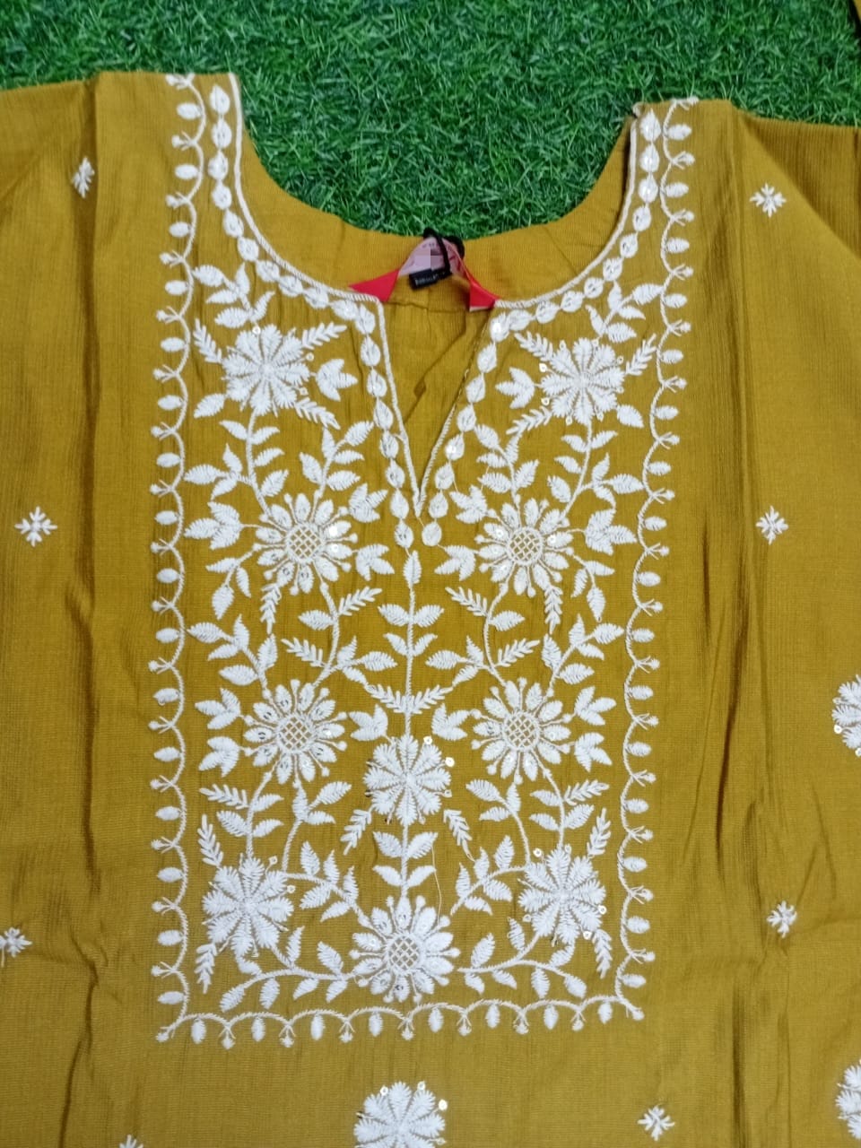 Mustard yellow kurta with white floral embroidery on a green grass background