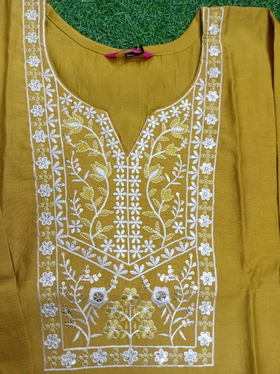 Mustard yellow top with white floral embroidery on a green background