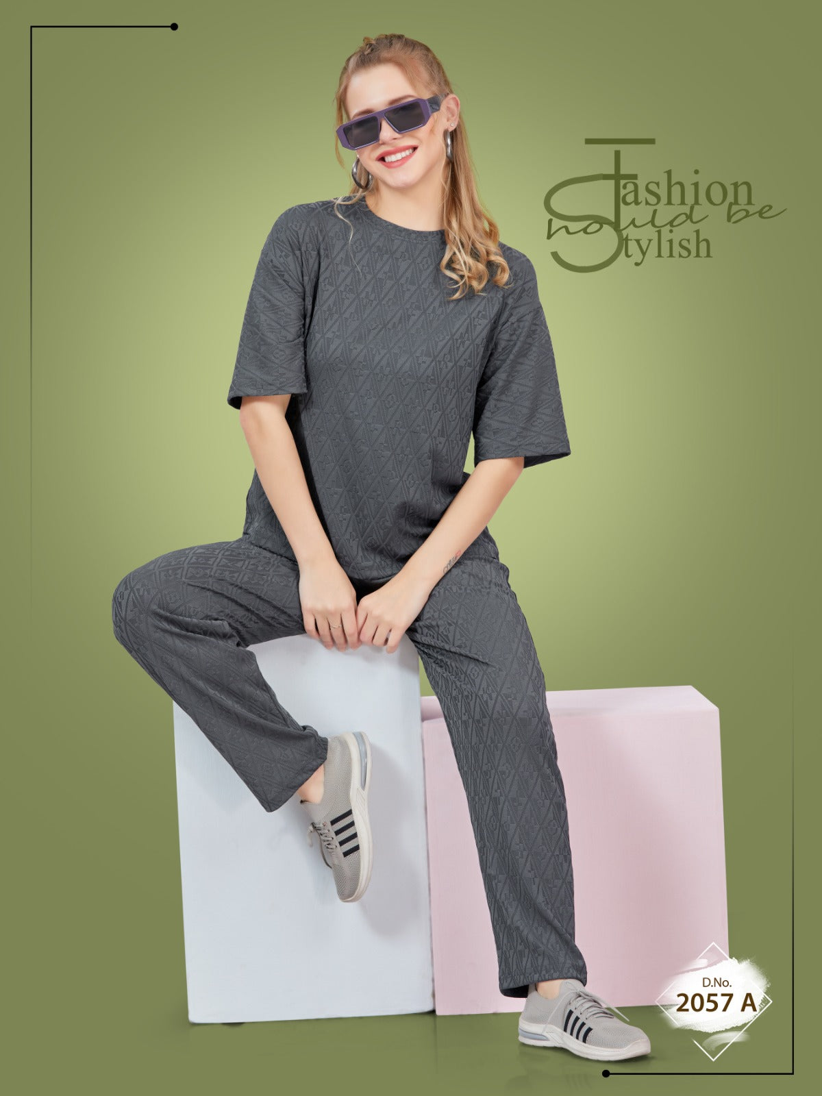 Woman wearing a gray outfit sitting on a pink and white block against a green background with 'Fashion is just a click' text.