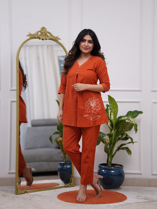 Woman in an orange outfit standing in a room with a mirror and plants.