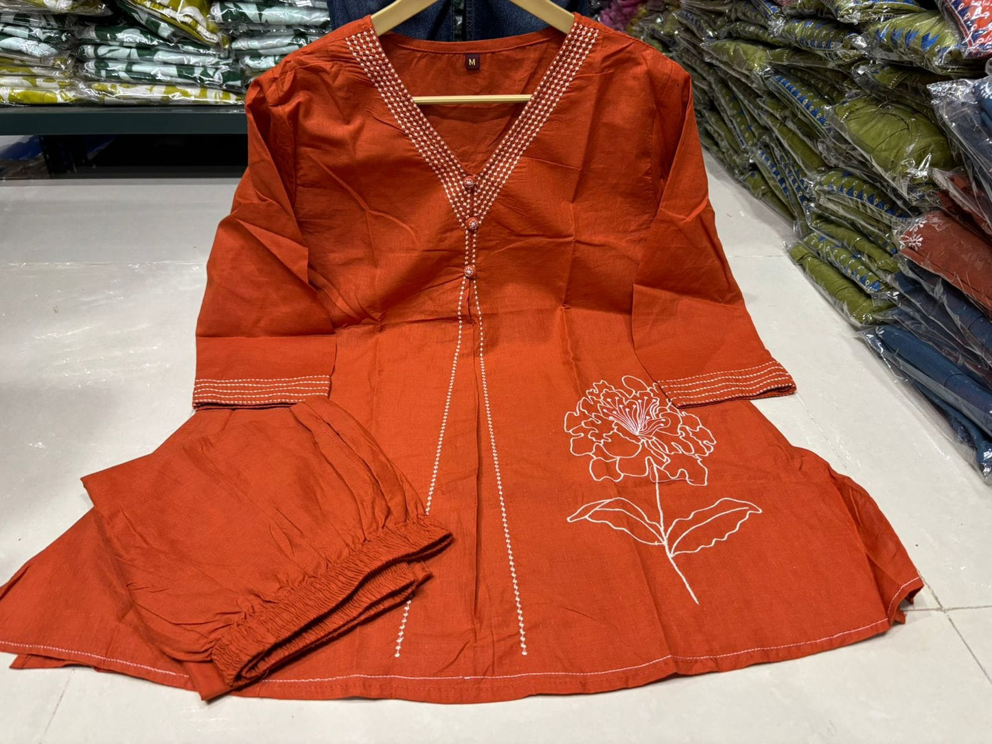 Orange dress with floral embroidery on a hanger in a store setting