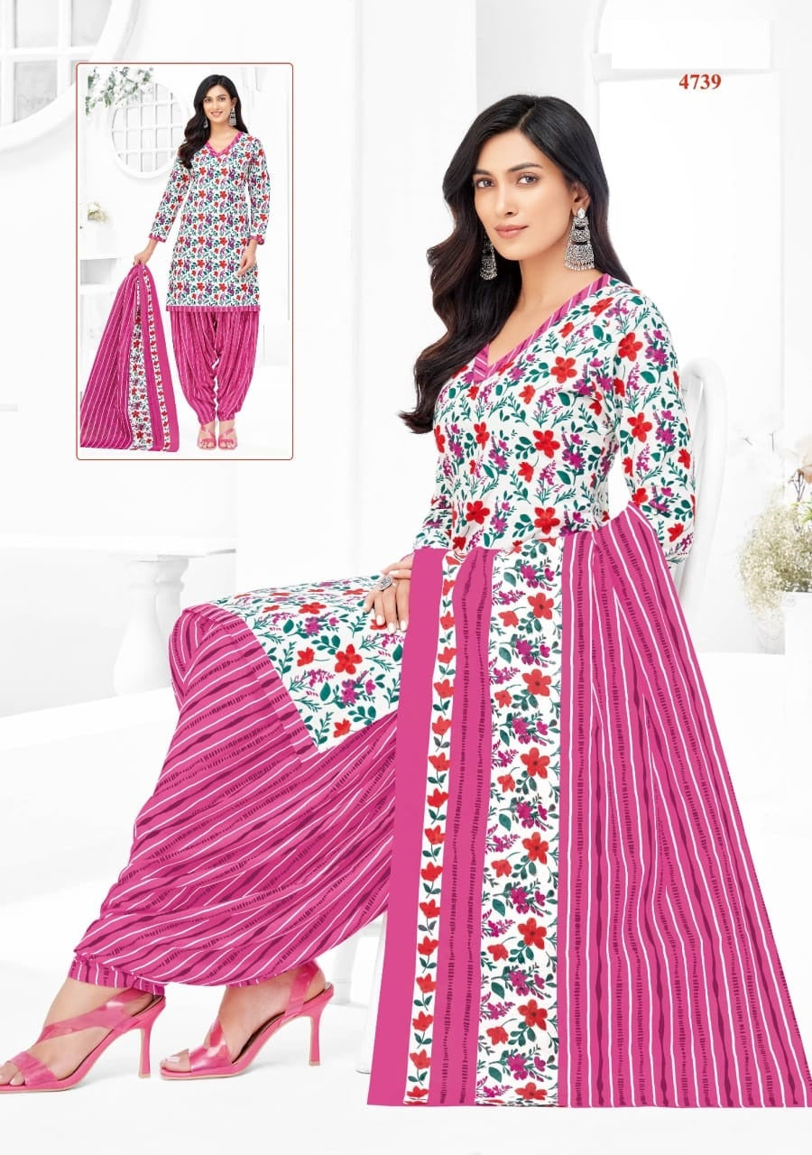 Woman wearing a floral and striped outfit with a pink dupatta, sitting on a white couch.
