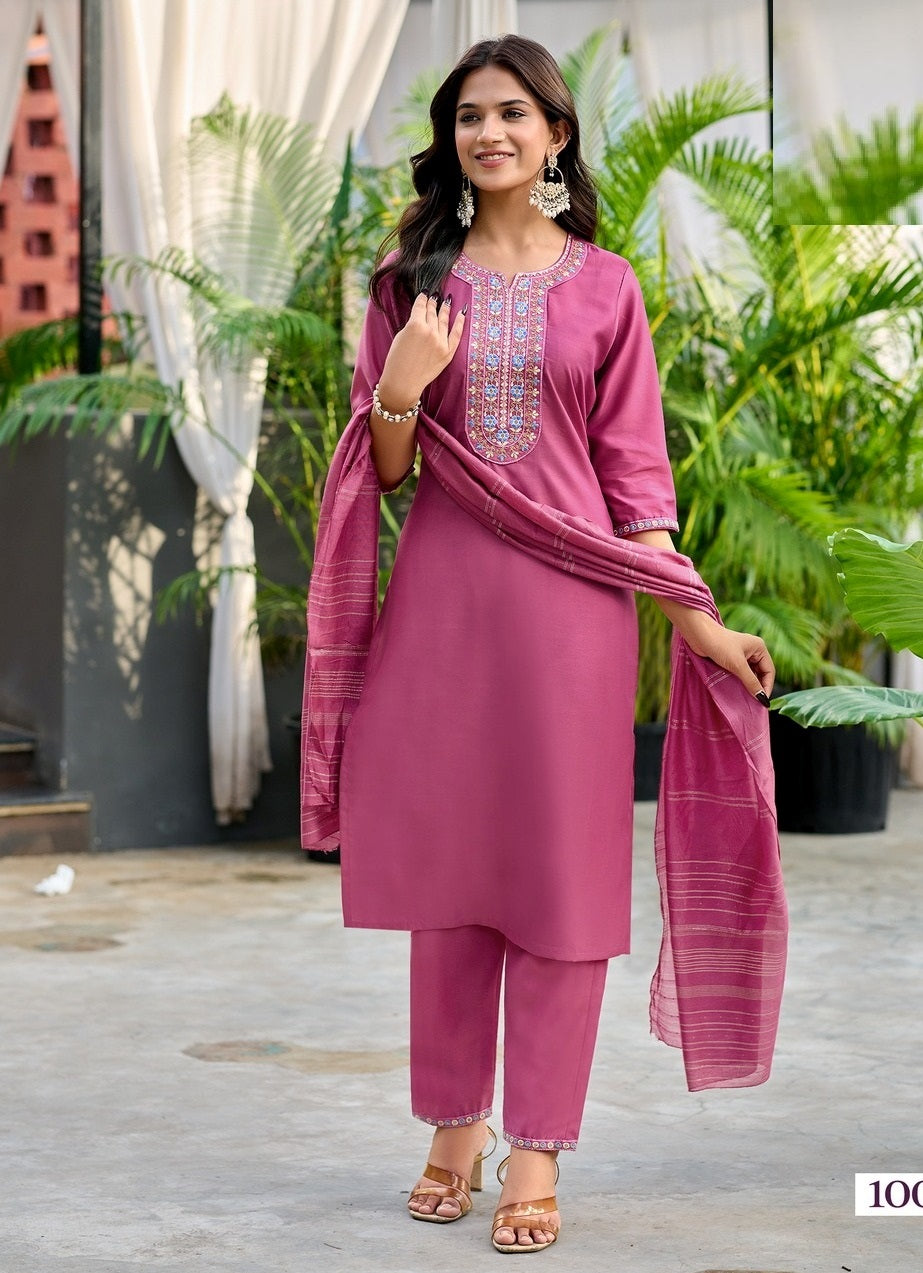 Woman in a pink traditional outfit with a dupatta, standing outdoors with plants in the background.