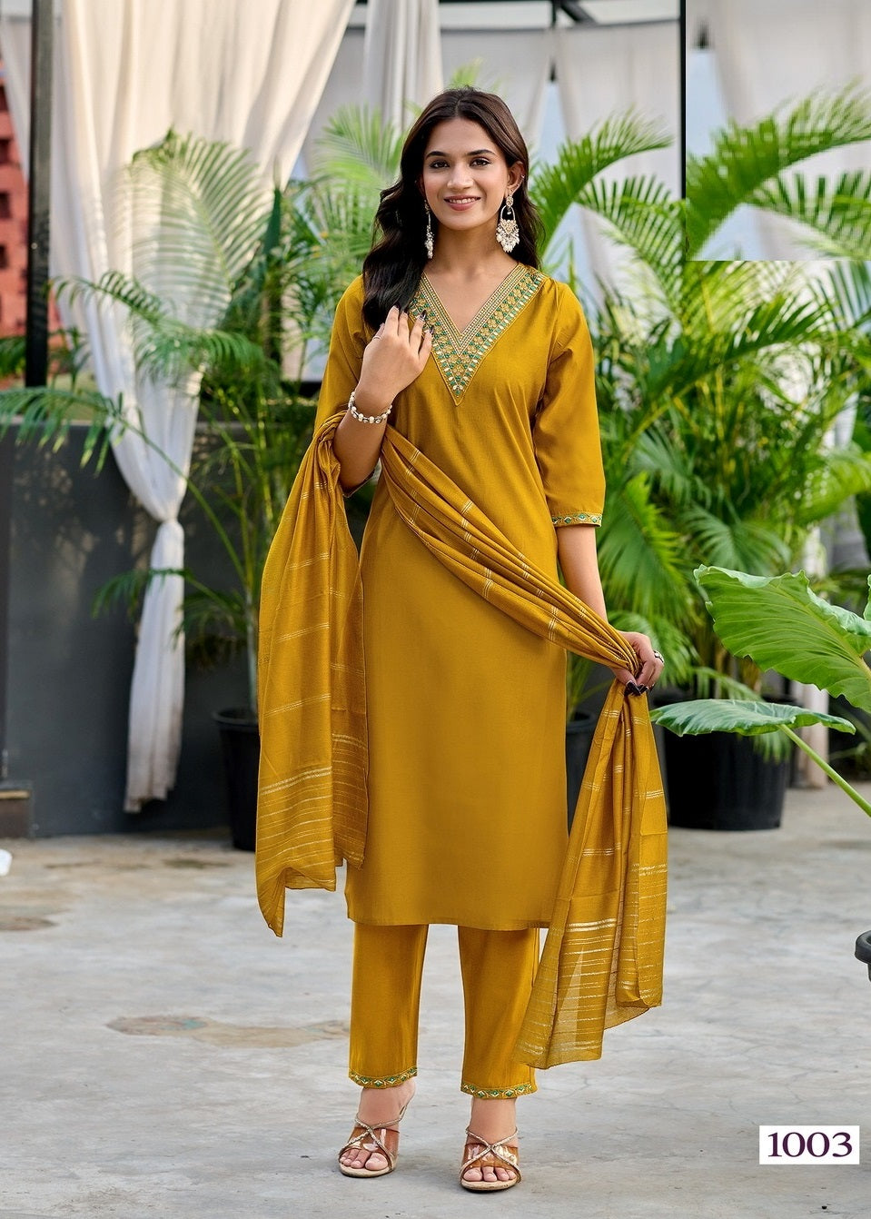 Woman in a mustard yellow traditional outfit standing outdoors with plants in the background