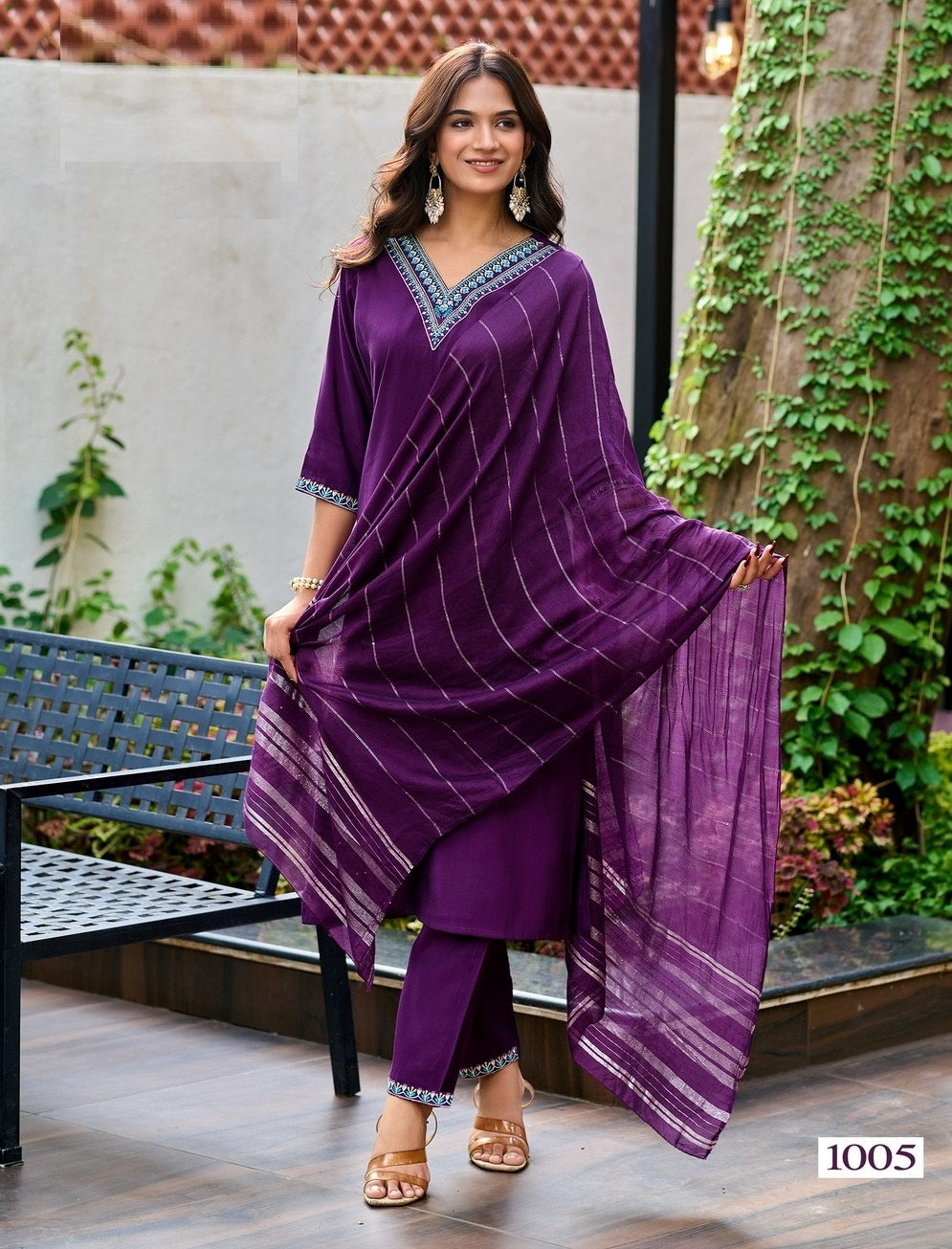 Woman wearing a purple traditional outfit with a patterned border, standing outdoors.