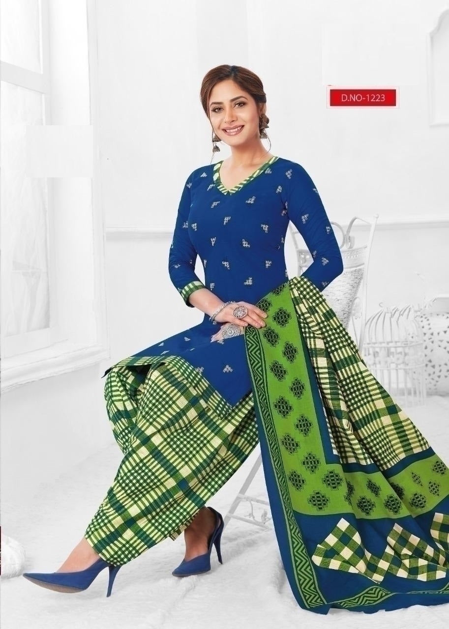 A woman sitting wearing a blue and green cotton fully stitched suit with a floral pattern and geometric design on the dupatta.